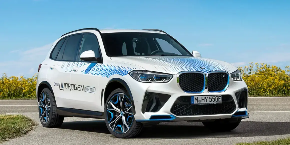 Białe BMW X5 z niebieskimi akcentami i napisem "BMW HYDROGEN FUEL CELL" na drzwiach, symbolizujące przyszłość motoryzacji.
