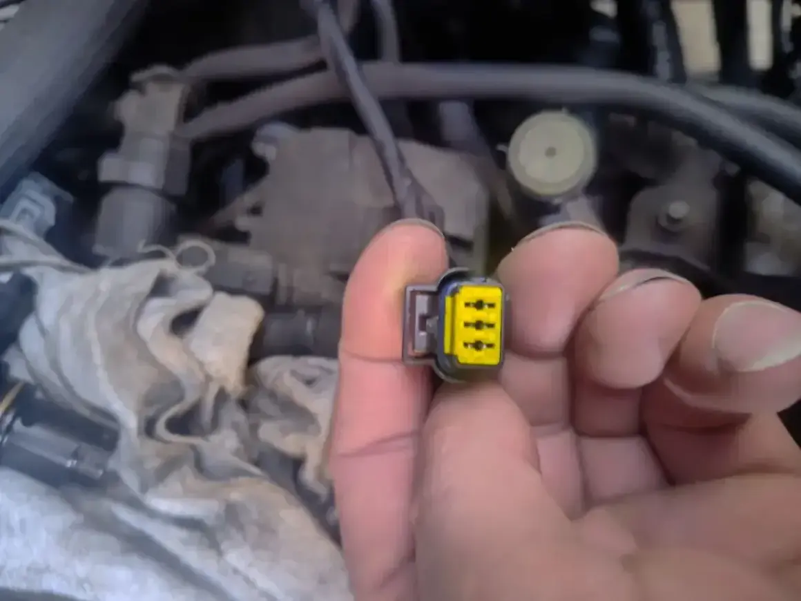 Wtyczka z żółtym wkładem, być może związana z błędem **dtc p1693 volkswagen**. W tle widać fragmenty silnika.