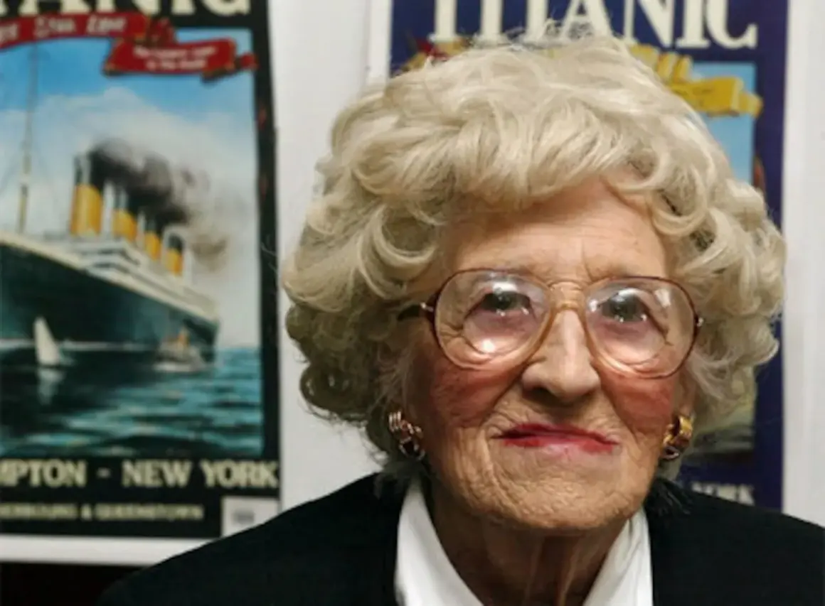 Una anciana con gafas grandes sonríe. Detrás de ella, carteles del Titanic, evocando a los supervivientes del trágico viaje.