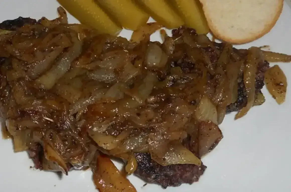 Pyszna kaszanka z patelni, duszona z cebulką, podana z ogórkiem kiszonym i kromką chleba.