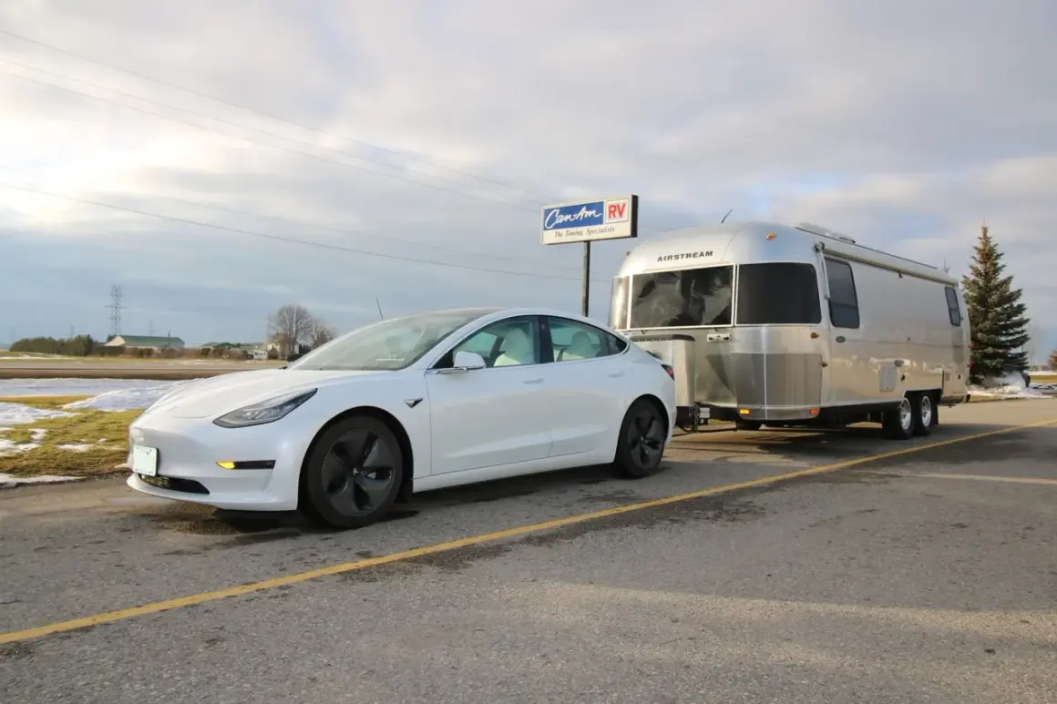 Une voiture électrique blanche tracte une caravane Airstream argentée. La question "peut on tracter avec une voiture electrique" trouve ici une réponse visuelle.