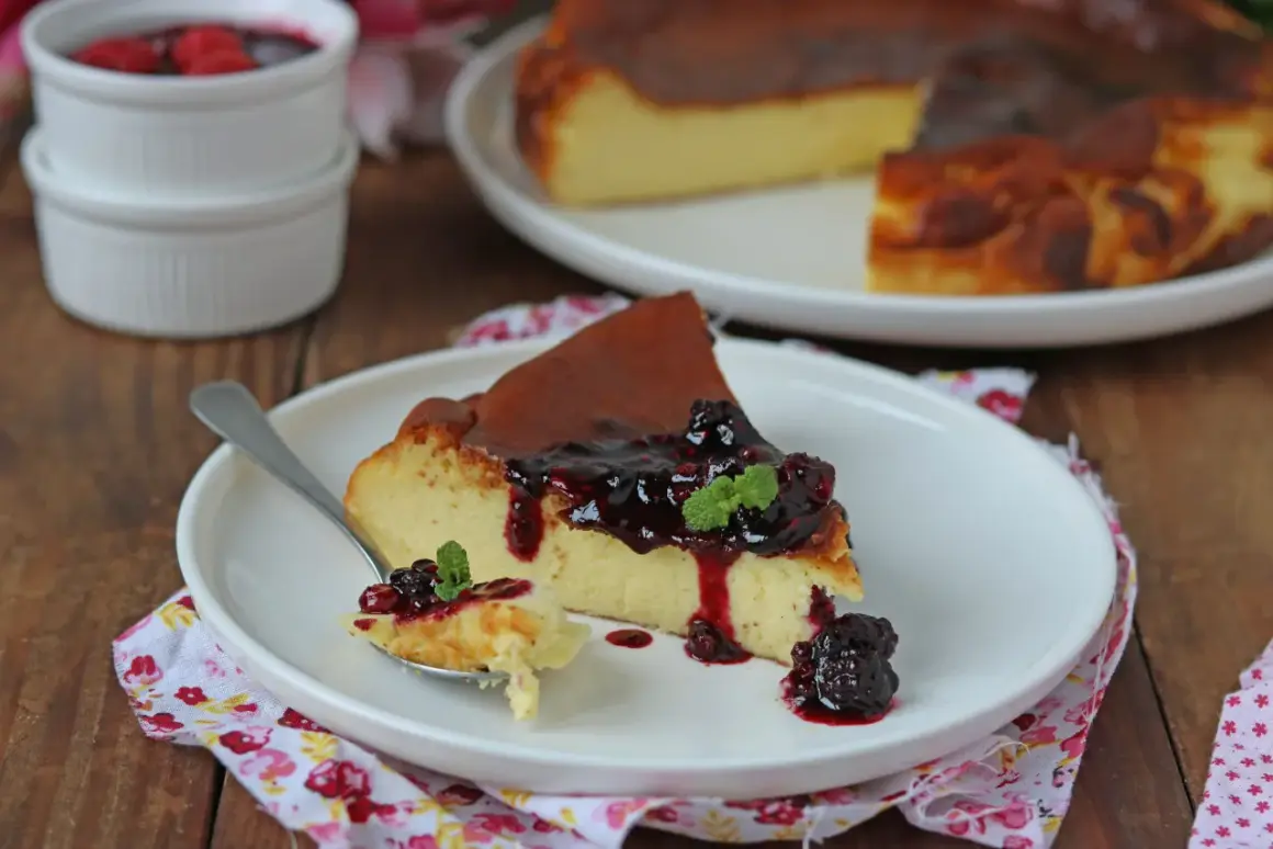 Una fetta di cheesecake basca cremosa, con topping di frutti di bosco e menta, su un piatto bianco.
