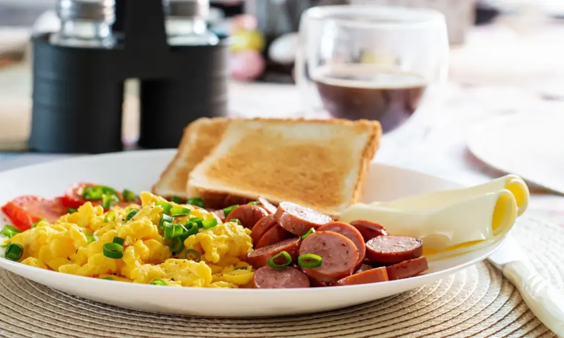 Un délicieux petit déjeuner sain avec des œufs brouillés, des saucisses, des toasts et du fromage.