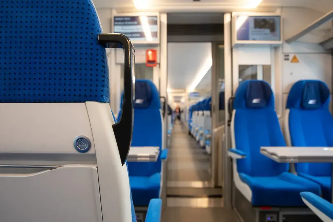 Wnętrze pociągu Pendolino. Widok na rzędy niebieskich foteli i stoliki. Wygodne wagony czekają na pasażerów.