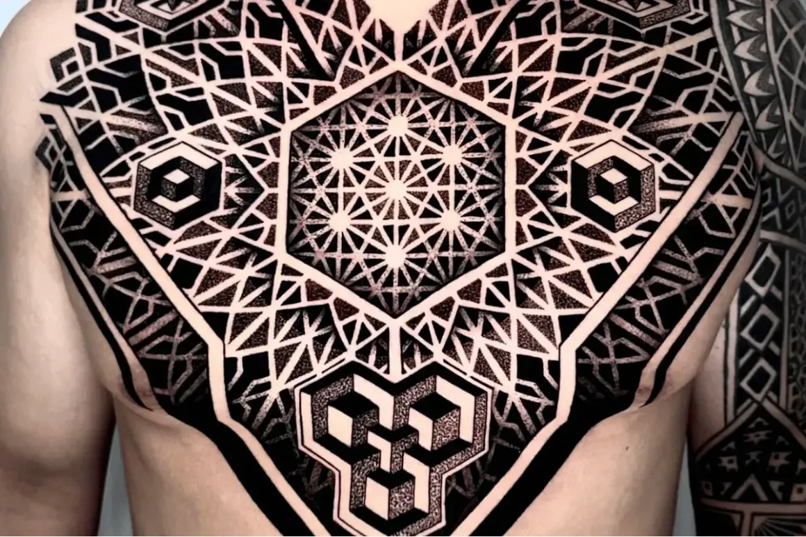 Ein komplexes Tattoo mit geometrischen Mustern bedeckt die Brust und den Arm. Es zeigt verschachtelte Hexagone, Würfel und stilisierte Dreiecke.