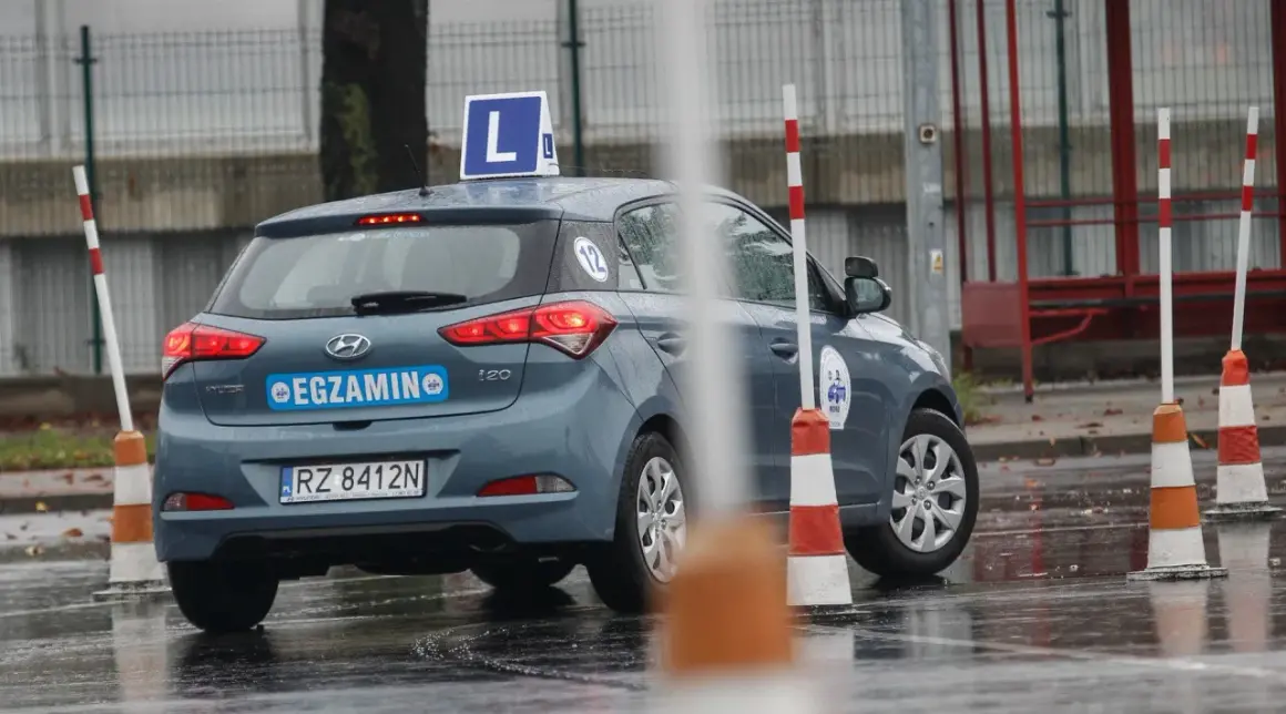 Szary Hyundai i20 z literą "L" na dachu i napisem "EGZAMIN" na klapie, gotowy do jazdy próbnej.