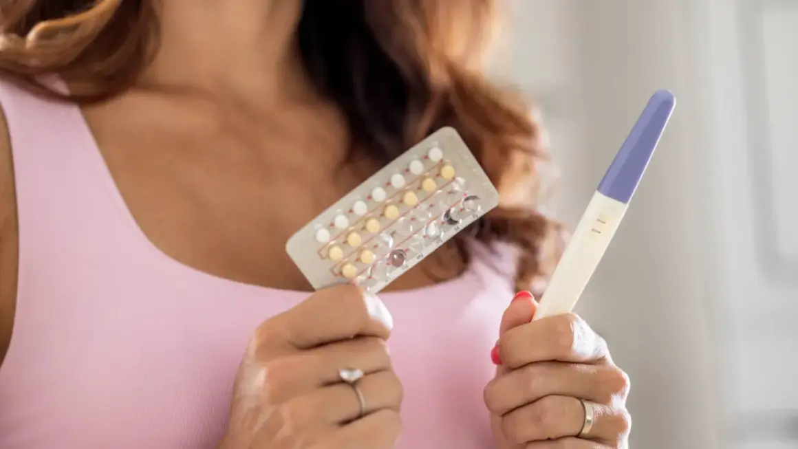 Donna tiene in mano un blister di pillole anticoncezionali e un test di gravidanza positivo. Si interroga su come rimanere incinta con la pillola e sui sintomi.