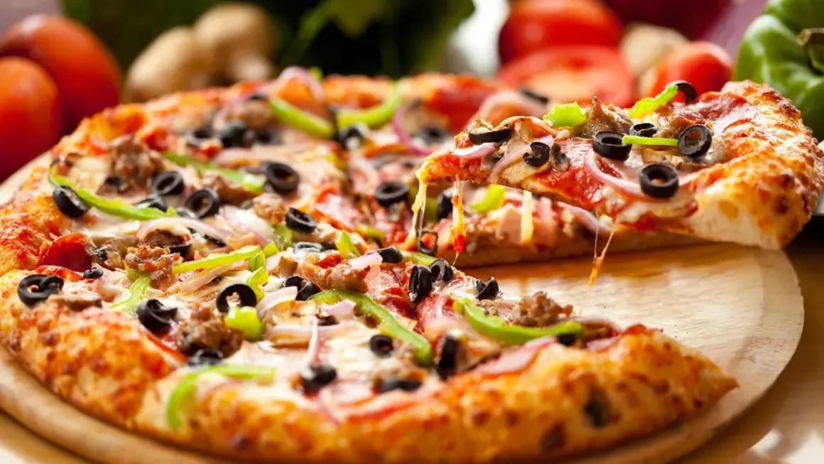 Gotowa pizza z ciągnącym serem, oliwkami, papryką i cebulą na drewnianej desce.