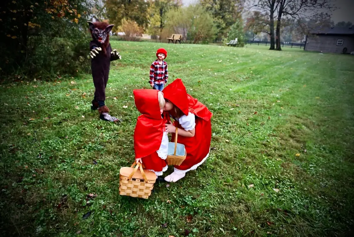 Dzieci w strojach Czerwonego Kapturka i wilk na trawiastym podwórku.