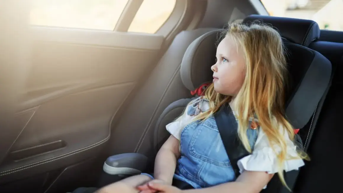 Ein blondes Mädchen sitzt im Kindersitz und schaut aus dem Fenster. Die Frage "wie lange Kindersitz" beschäftigt viele Eltern.