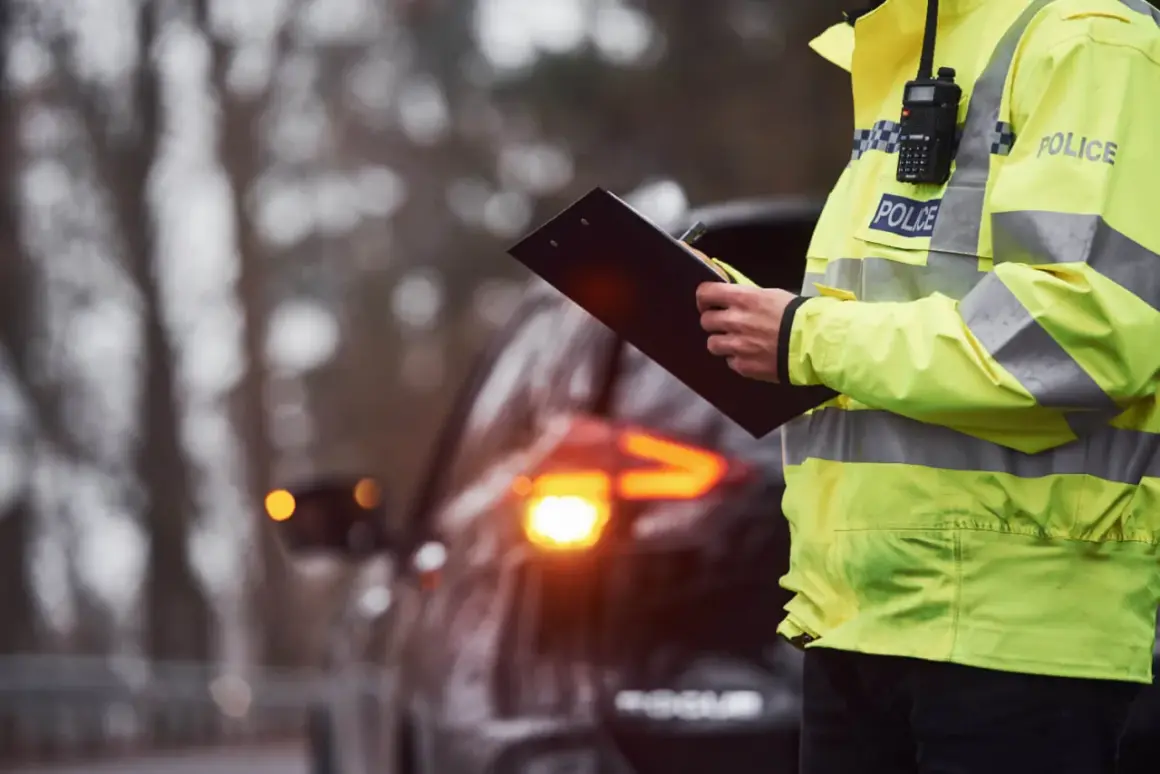 Policjant w kamizelce odblaskowej z napisem "POLICE" spisuje mandaty na Słowacji. W tle widać samochód z włączonymi światłami awaryjnymi.