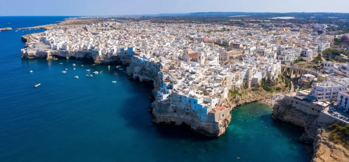 Vista aerea di Polignano a Mare, con le case bianche a picco sul mare blu intenso. Un gioiello della Valle d'Itria, dove il mare incontra la terra.