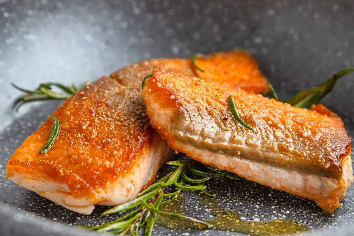 Zwei saftige Lachsfilets mit knuspriger Haut, perfekt gebraten, liegen in einer Pfanne mit Rosmarin und Öl.
