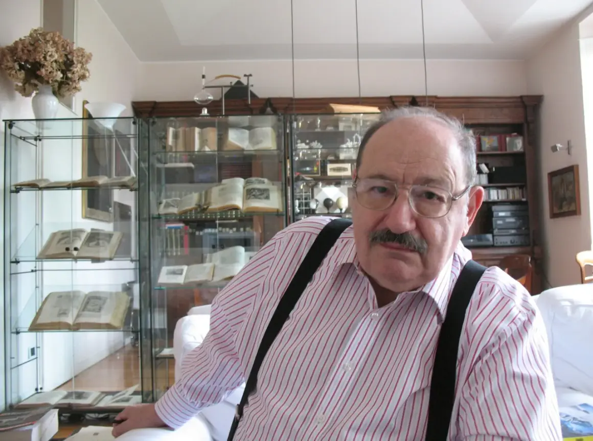 Wilhelm z Baskerville, w okularach i koszuli w paski, siedzi w otoczeniu antycznych ksiąg i gabinetów pełnych skarbów.
