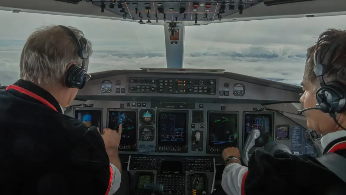 Dwóch pilotów w kokpicie, jeden wskazuje na ekran. Zastanawiasz się, ile zarabia pilot? To praca pełna odpowiedzialności.
