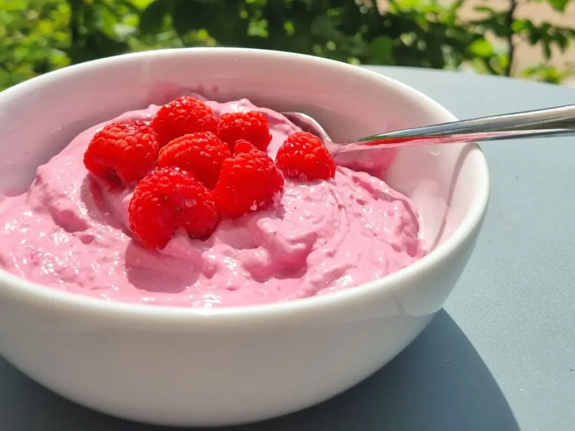 En skål med rosa krämig dessert toppad med färska hallon. Perfekt för nyttiga snacks en solig dag.
