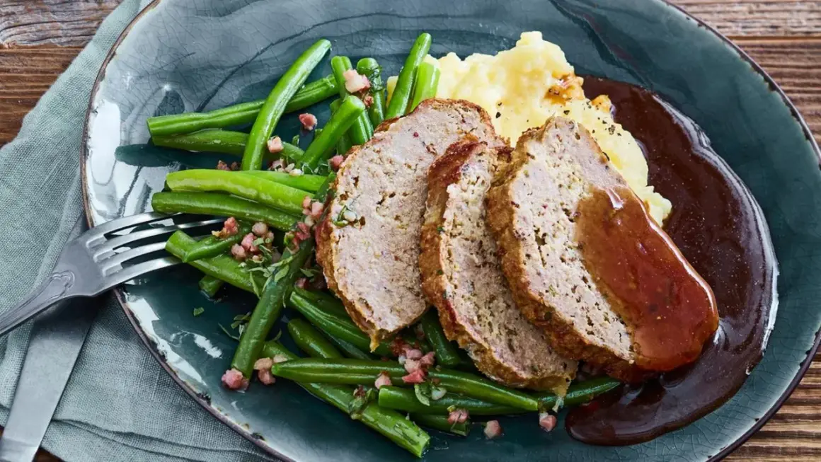 Saftiger hackbraten im ofen, serviert mit grünen Bohnen und Kartoffelpüree, übergossen mit dunkler Soße.