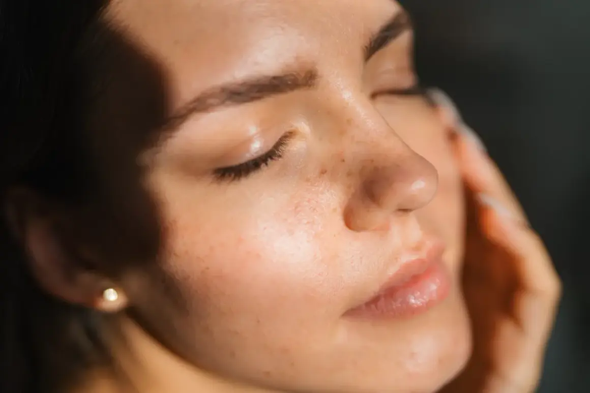 Viso di donna con lentiggini, illuminato da luce soffusa. La pelle appare curata, suggerendo che retinolo e vitamina C si possono usare insieme per un incarnato radioso.