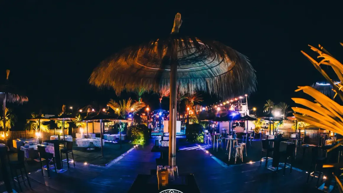 Noche vibrante en el chiringuito Macenas. Sombrillas de paja, luces de colores y mesas listas para disfrutar.