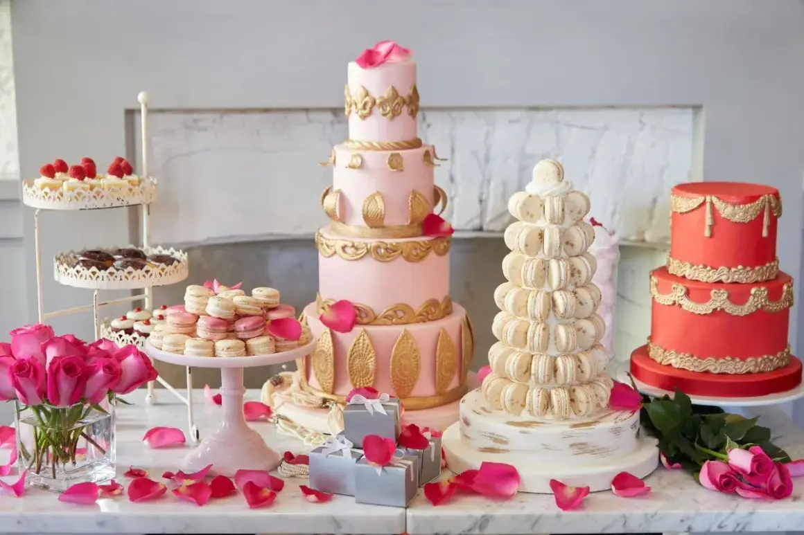 Ein prachtvolles Kuchenbuffet für eine Hochzeit: mehrstöckige Torten in Rosa und Rot, Macarons-Türme und Rosen.