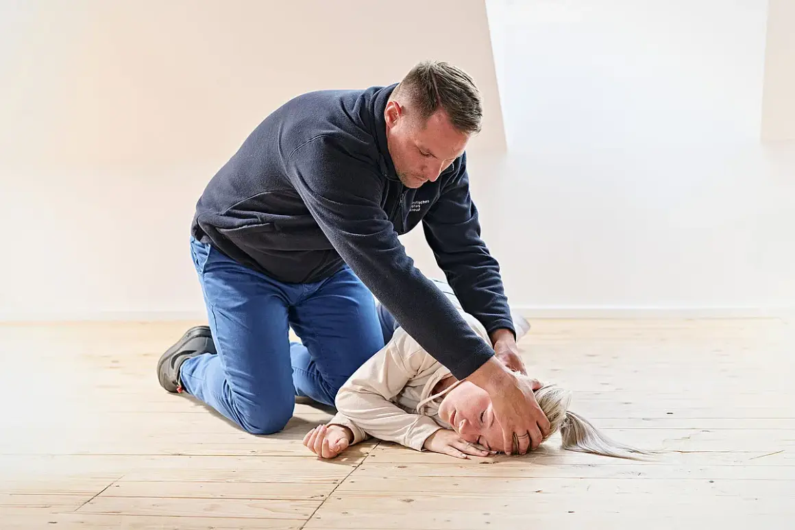 Mann übt stabile Seitenlage an einer liegenden Person. Die Person liegt auf der rechten Seite, der Kopf ist nach hinten geneigt.