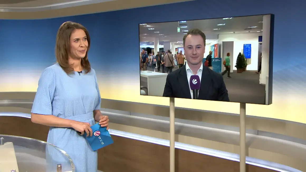 Moderatorin hält Umschlag mit Logo von tv-n hessen. Auf dem Bildschirm ein Reporter im Anzug.