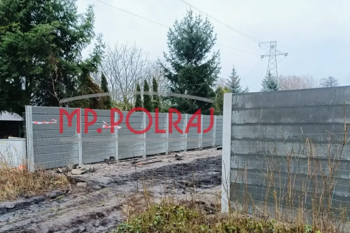 Solidne, betonowe ogrodzenie 2 metry wysokości, z napisem MP. POLRAJ, otacza teren.
