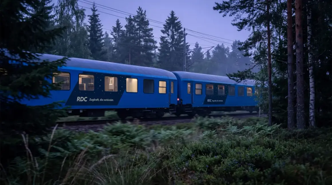 Blått nattåg från RDC passerar genom en skog i skymningen. Tåget är på väg mot Berlin, en resa som börjar i Sverige.