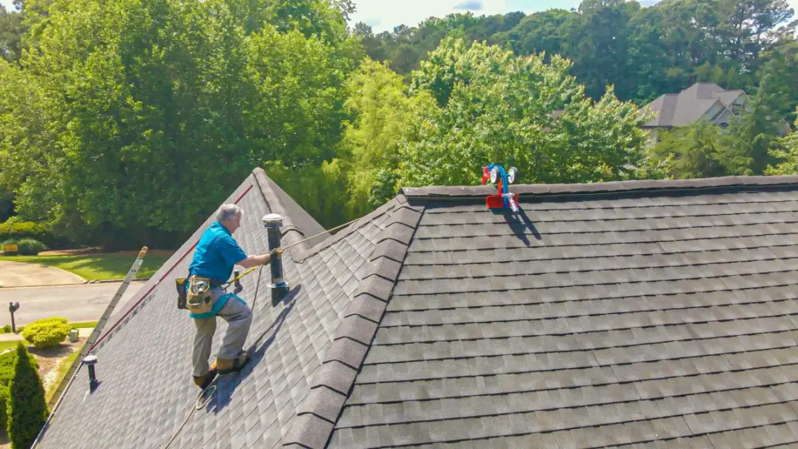 A roofer demonstrates how to shingle a steep roof, using safety gear and a ladder.