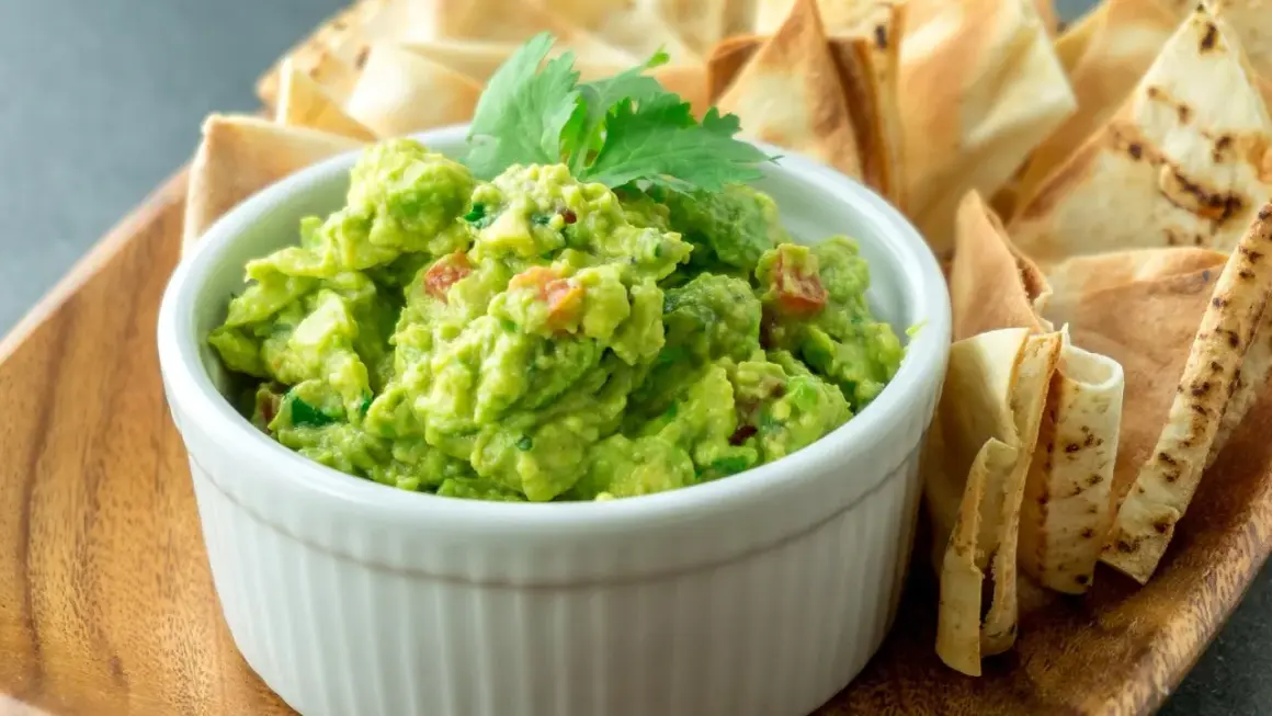 Pyszne guacamole z pomidorami i kolendrą, idealne do szybkiego przygotowania. Podane z chrupiącymi nachos.