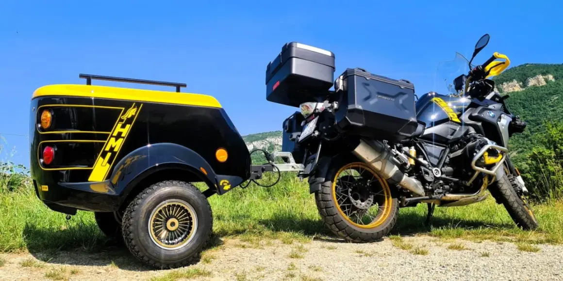 Une remorque pour chien moto, noire et jaune, est attelée à une moto BMW tout-terrain, prête pour une aventure en plein air.