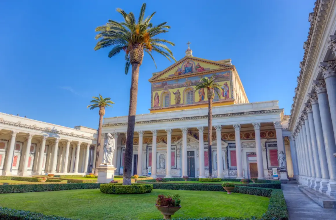 Giardino curato davanti alla Basilica San Paolo, con palme alte e statue.
