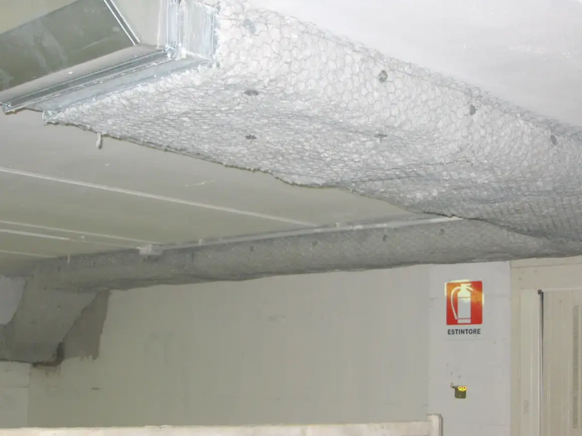 Condotti metallici coperti da rete e materiale isolante, con segnale di estintore. La pittura ignifuga protegge le strutture.