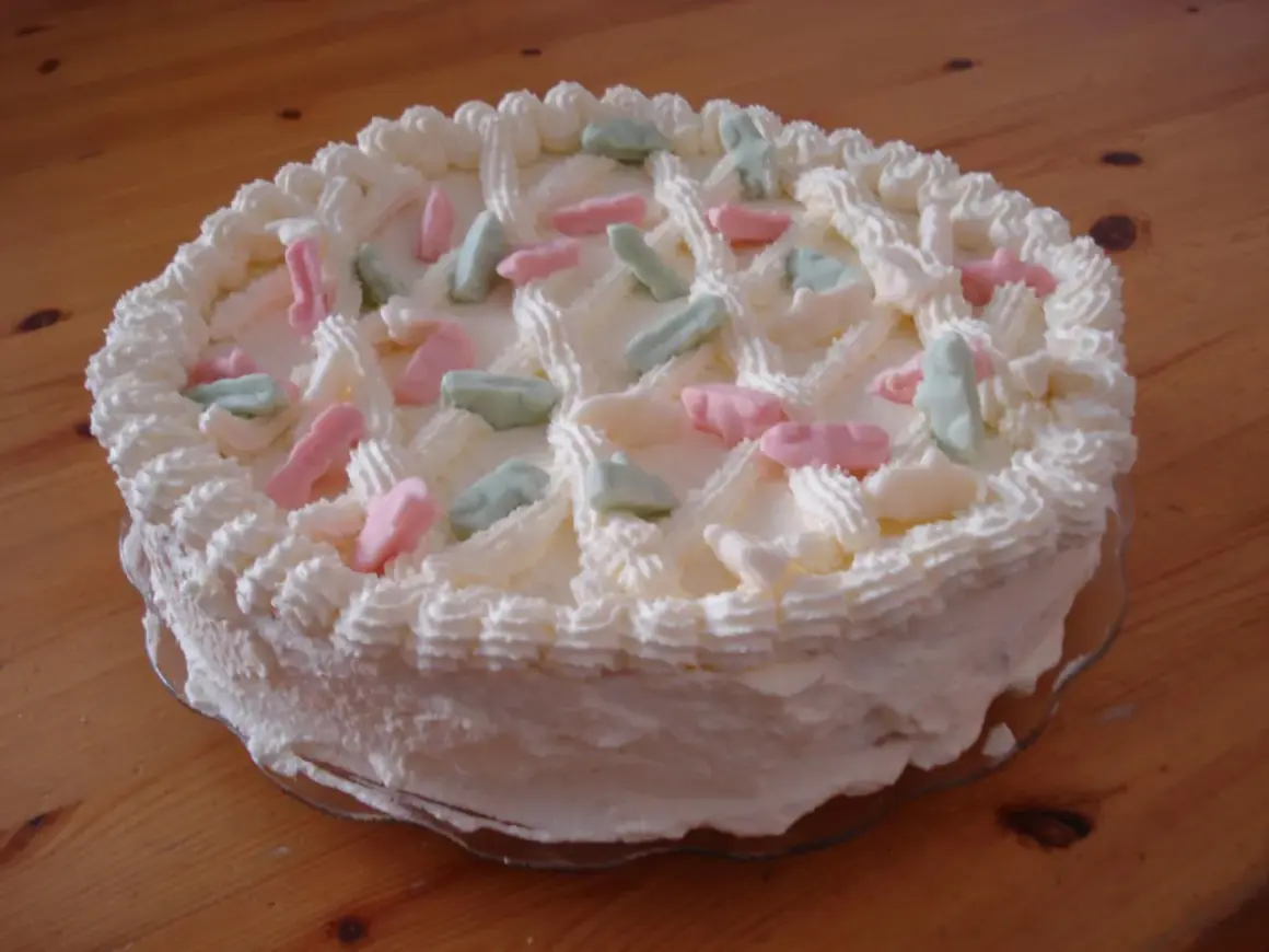 En vit gräddtårta dekorerad med rosa, gröna och vita Ahlgrens bilar. Perfekt för en festlig stund!