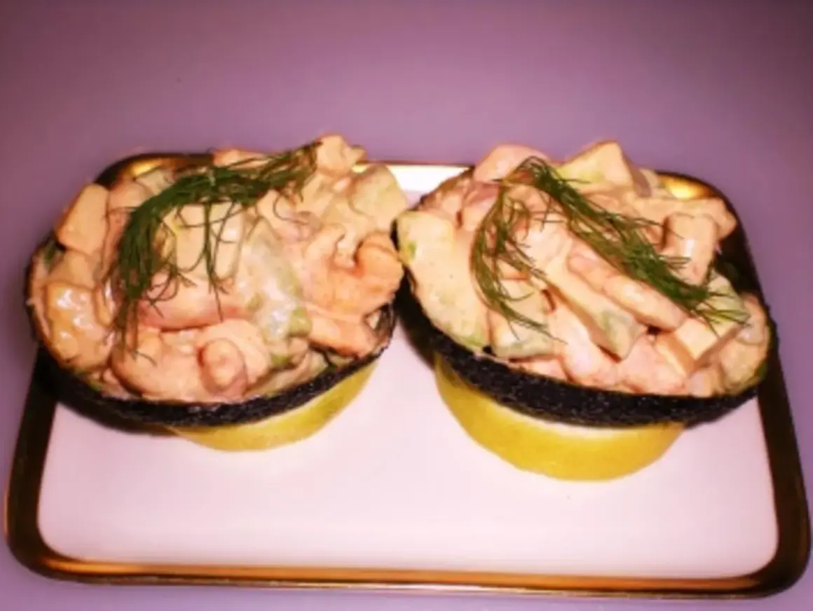 Zwei Avocadohälften gefüllt mit einem cremigen Krabbencocktail mit Avocado und Dill garniert, serviert auf Zitronenscheiben.