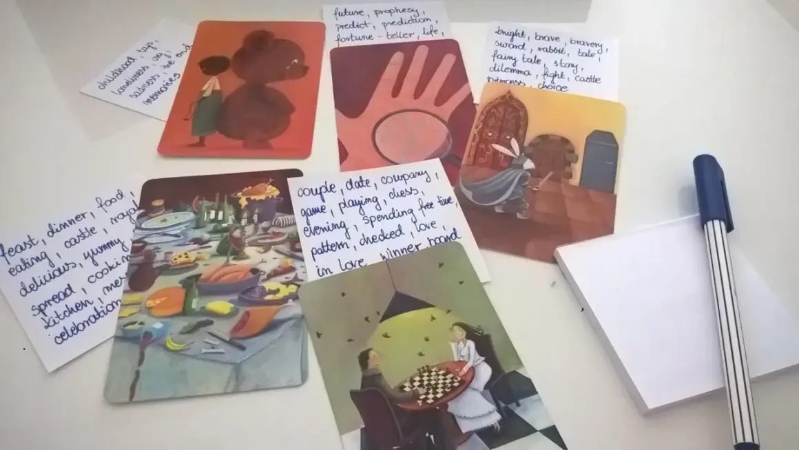 Karty z ilustracjami i notatki z hasłami: "dixit pomysły na hasła", uczta, rycerz, dzieciństwo, para grająca w szachy.