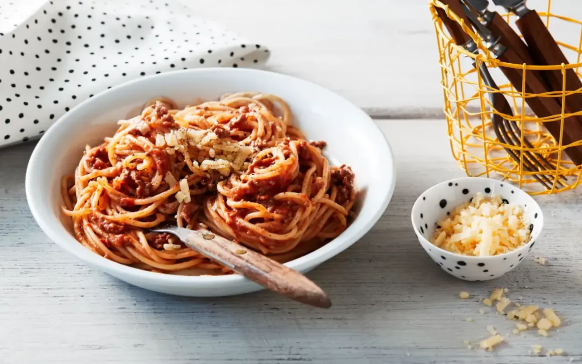 Ein Teller Spaghetti Bolognese, ein Klassiker unter den spaghetti rezepte, mit geriebenem Käse bestreut. Daneben eine Schale mit extra Käse.