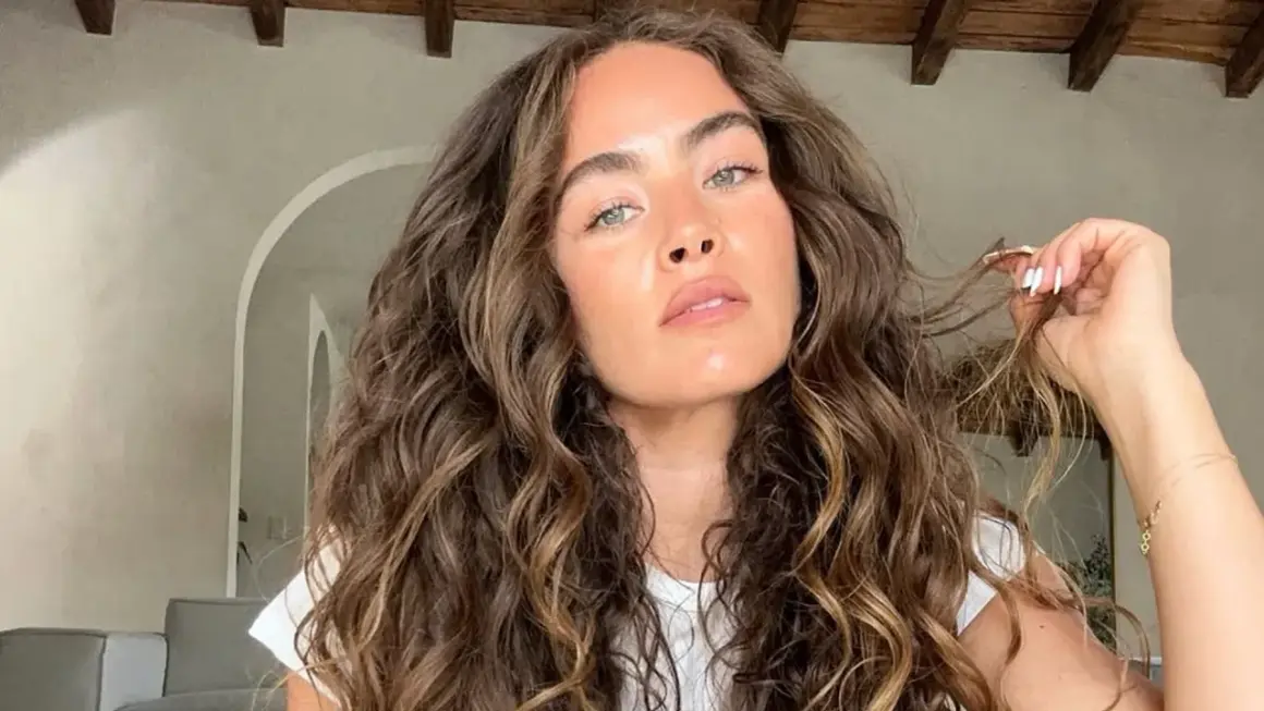 Mujer con un espectacular pelo rizado castaño, con reflejos dorados, acariciando un mechón.