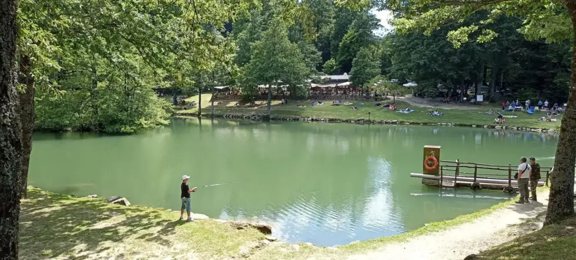 Un ragazzo pesca sul lago Pontini, mentre altre persone si rilassano sull'erba.