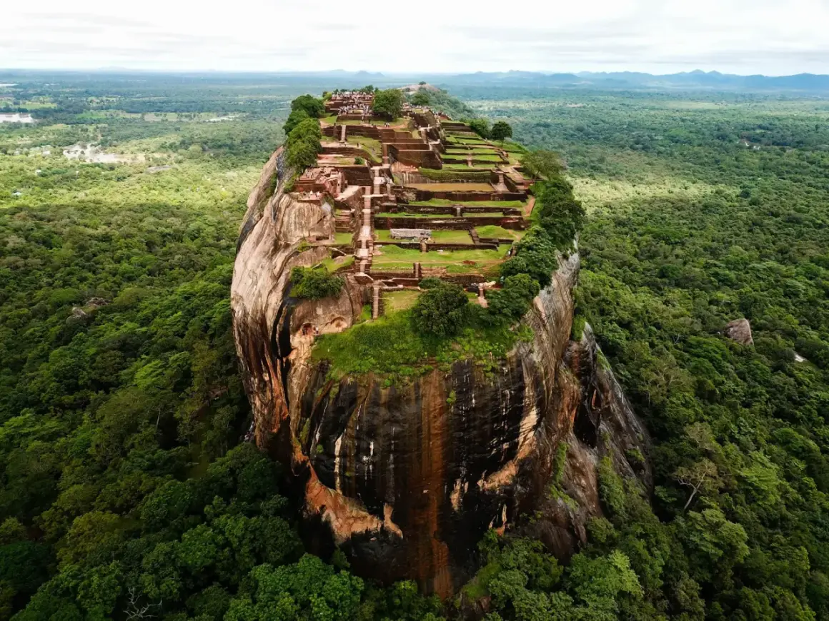 Imponerande ruiner på toppen av en klippa, som en fästning. En vy som påminner om Adams Peak, omgiven av frodig djungel.