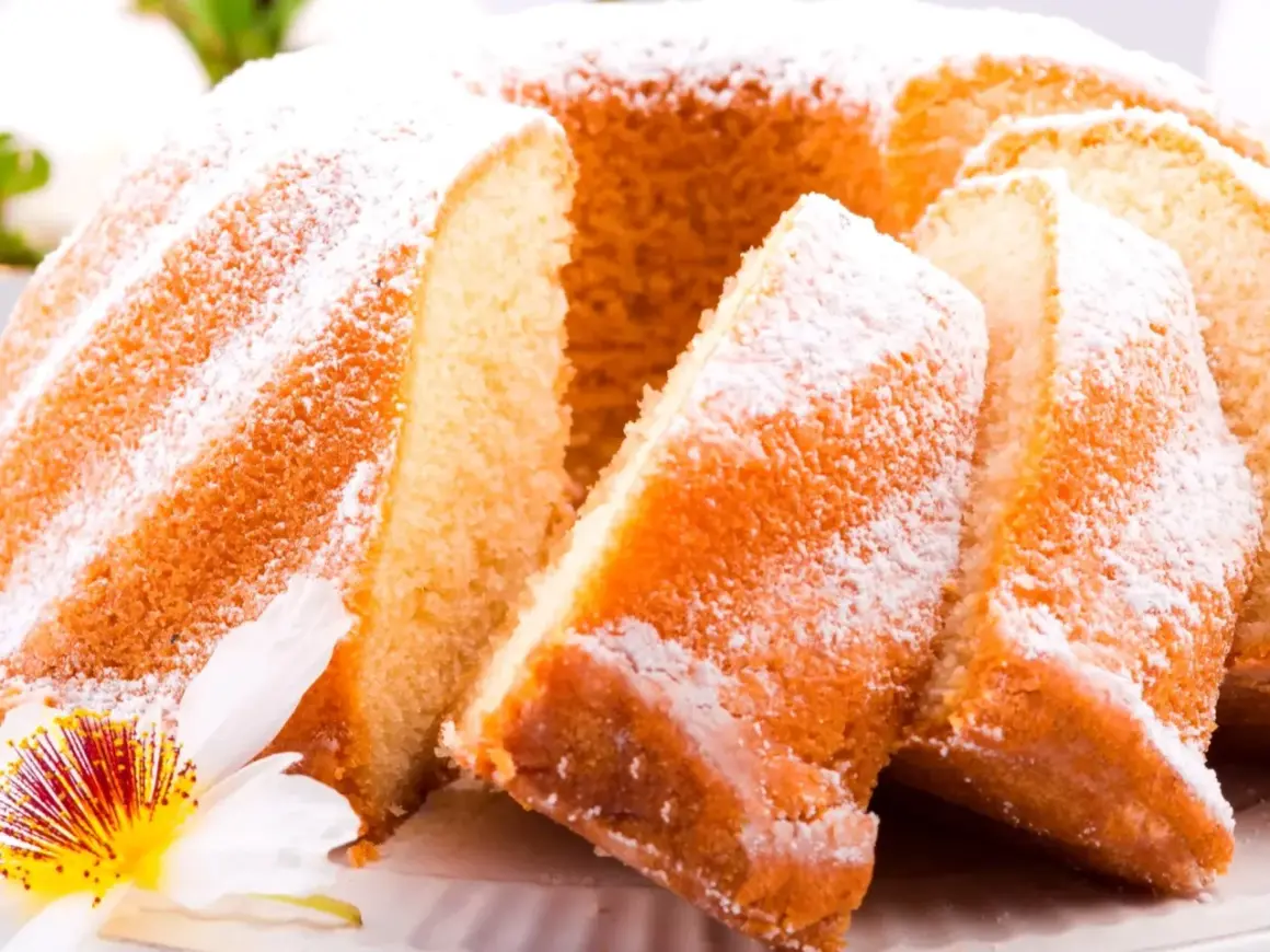 Puszysta babka wielkanocna, oprószona cukrem pudrem, z kawałkami ciasta i kwiatową dekoracją.