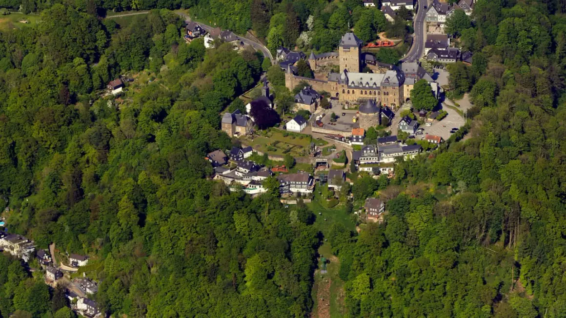Luftaufnahme eines Schlosses, eingebettet in grüne Wälder. Die Burg ist ein beliebter Ort für Veranstaltungen und Ausflüge.