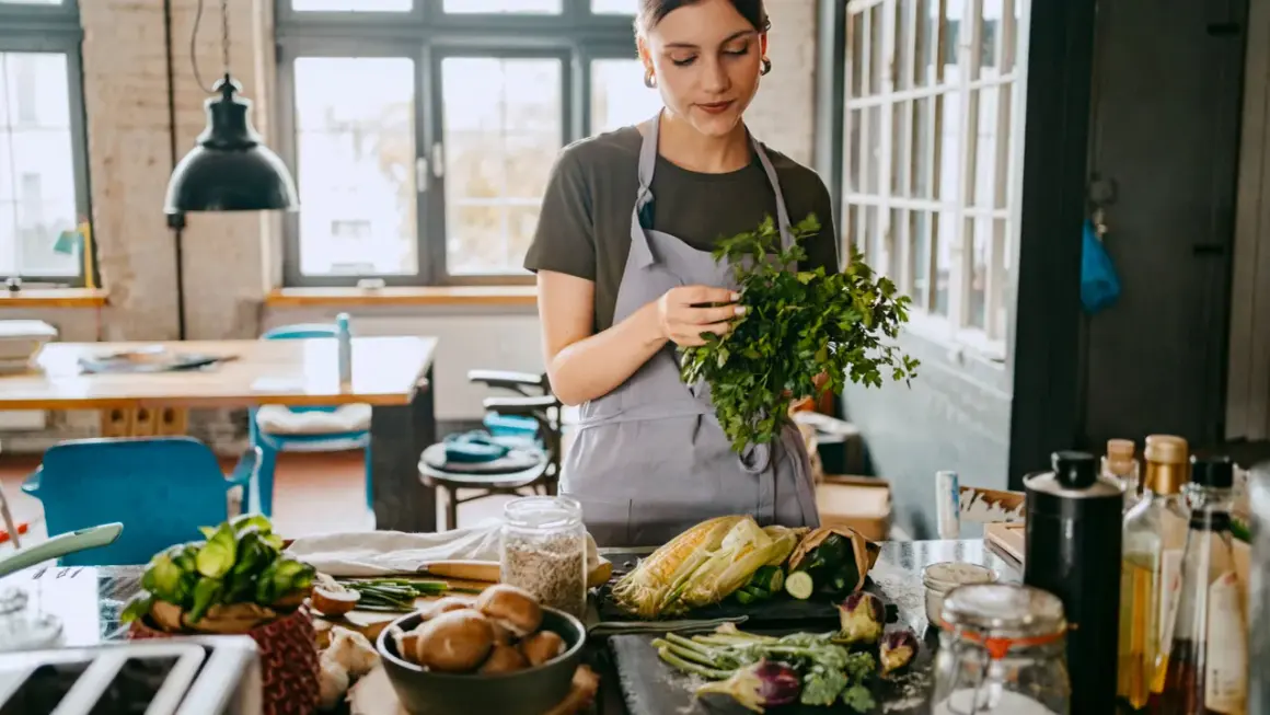 Frau bereitet frisches Gemüse für eine gesunde Ernährung zu. Kräuter, Mais und Pilze auf dem Tisch, inspiriert von der planetary health diet.