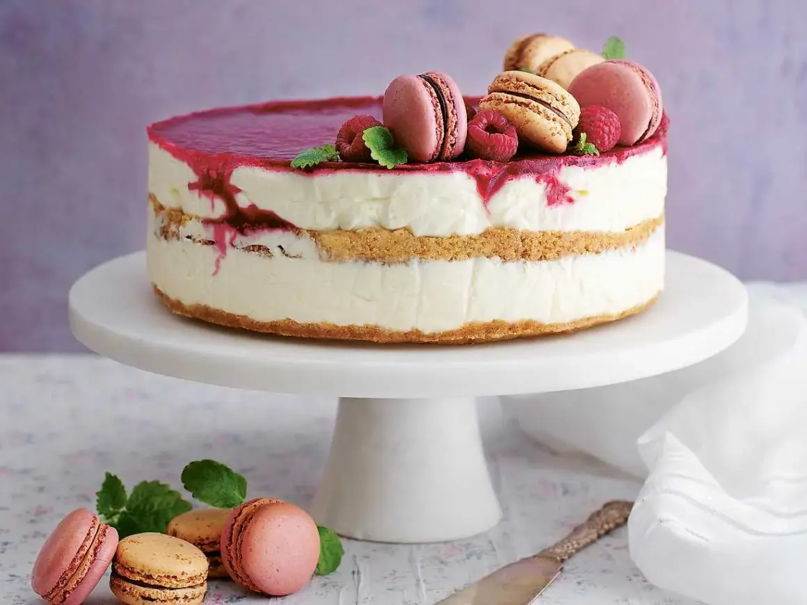 En vacker nyårstårta med lager av krämig fyllning, kexbotten och hallonspegel. Toppad med macarons, hallon och mynta. Ett perfekt nyårstårta recept!