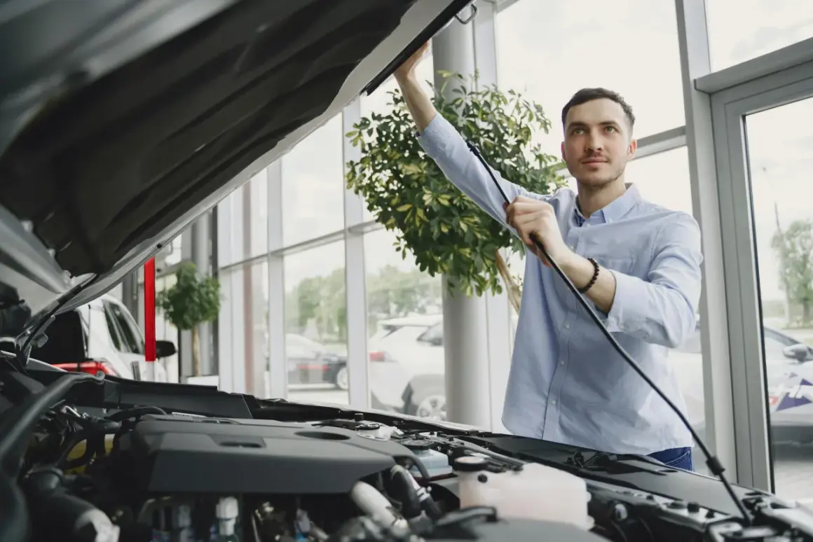 Un homme examine le moteur d'une voiture neuve dans un showroom. Il s'assure de la qualité avant de finaliser le prix de l'expertise voiture.