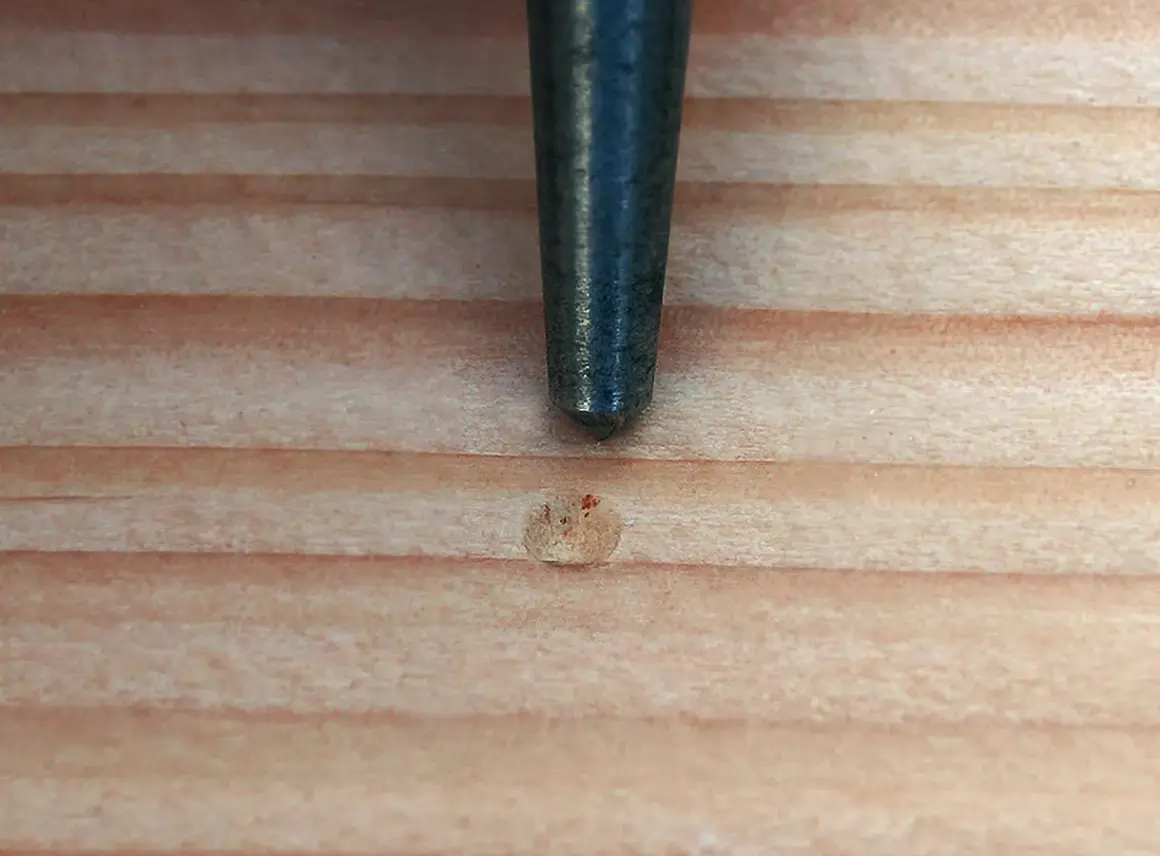 Ein Metallstift markiert eine Stelle auf Holz, bereit zum schamottstein bohren.