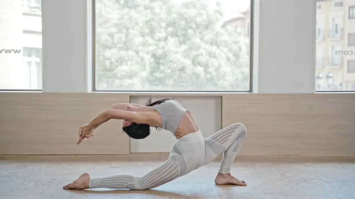 Mujer en postura de Anjaneyasana yoga, arqueando la espalda y extendiendo brazos hacia atrás.