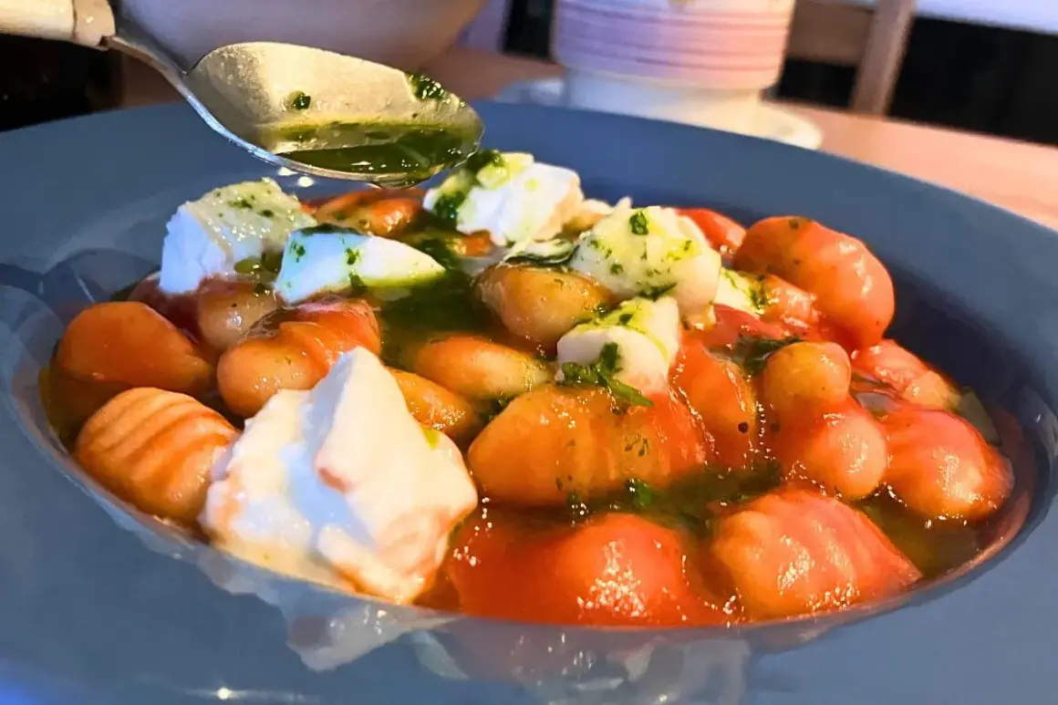 Pyszne makaron gnocchi z pomidorami, mozzarellą i zielonym sosem. Łyżka z sosem czeka na dodanie.