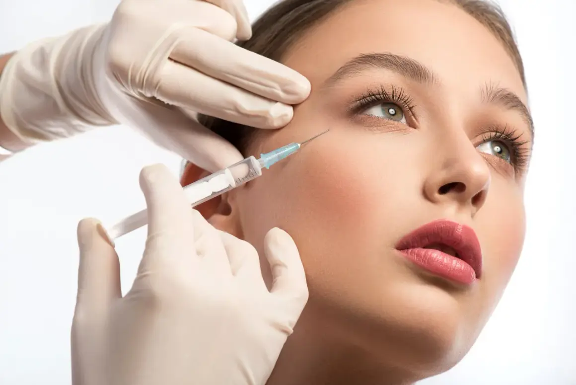Delikatna aplikacja baby botox w okolicę oka. Dłoń w rękawiczce trzyma strzykawkę, wykonując zabieg.