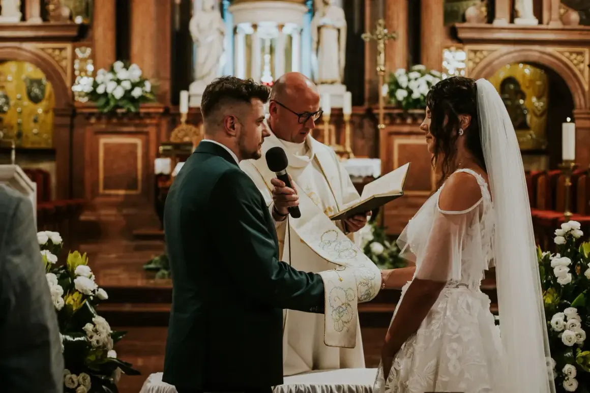 Para młoda i pan młody podczas ceremonii, łączącej ślub kościelny i cywilny razem. Ksiądz czyta z księgi.